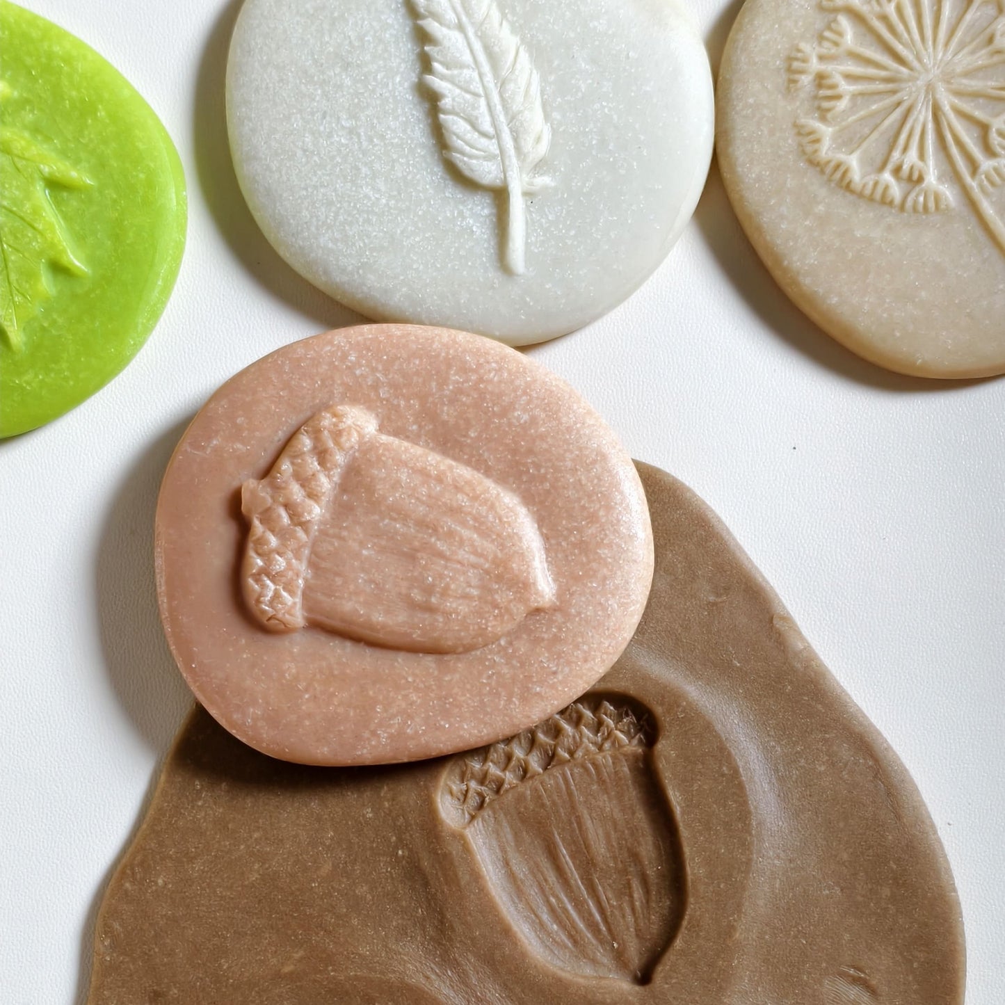 Primer plano de una piedra-sello dejando una huella profunda y detallada de una bellota y una piña en masa de juego marrón.